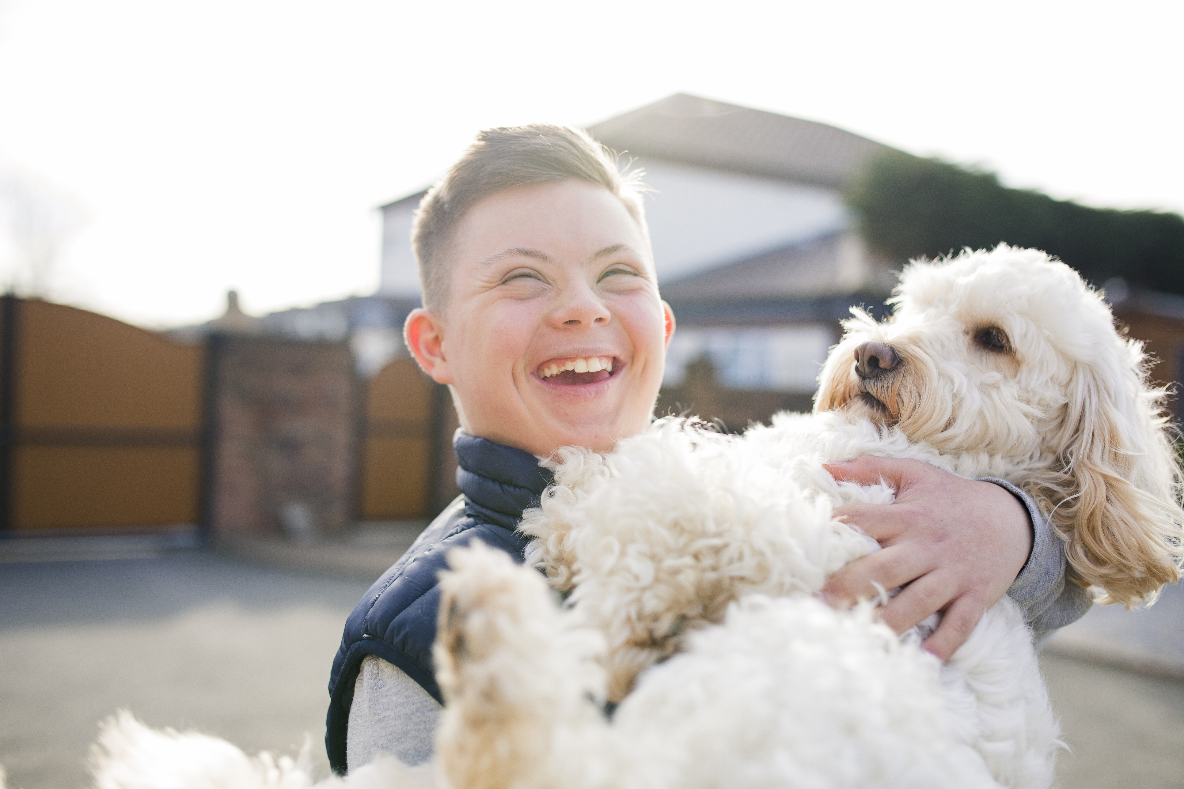 Young person with Down syndrome laughing outdoors with a dog